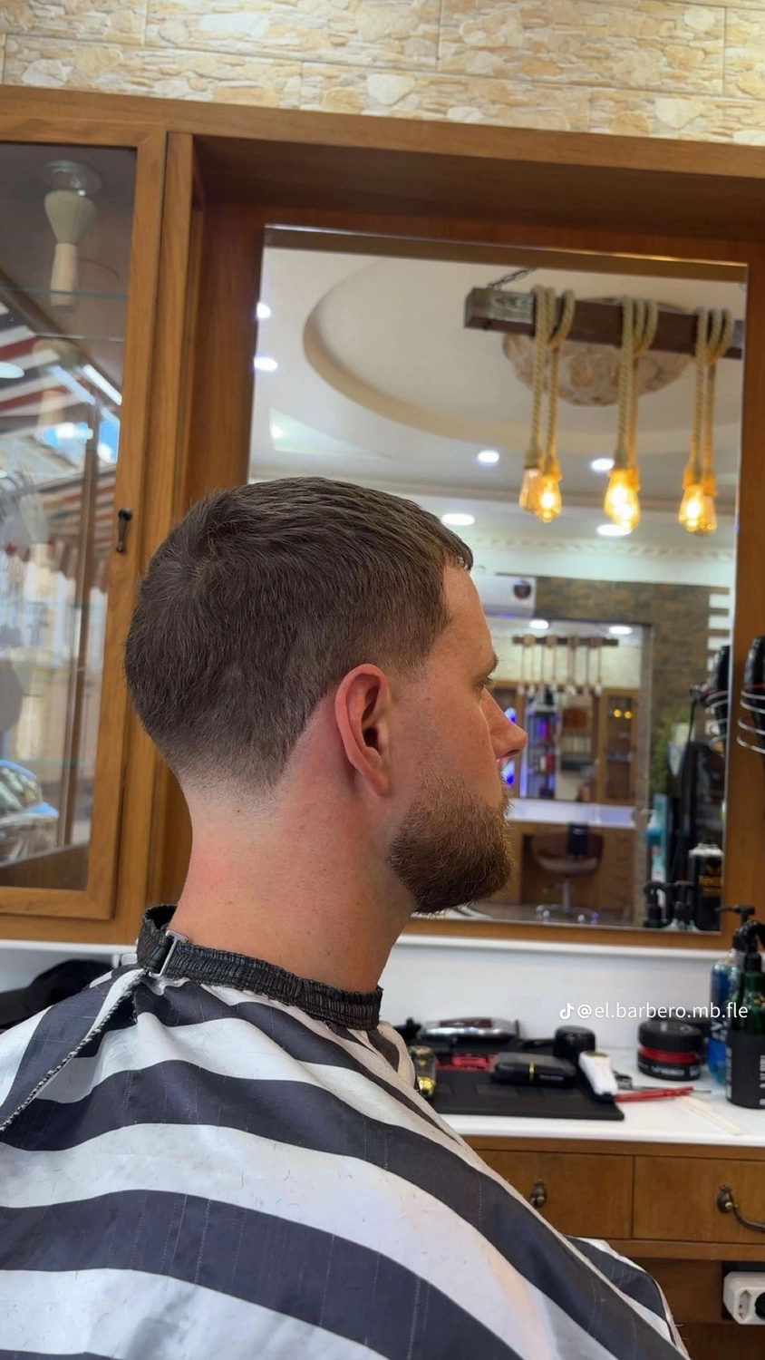El barbero MB - Haar- und Hautpflegebehandlungen - Seitenansicht eines Mannes mit einem präzisen Skin Fade-Haarschnitt und gepflegtem Bart im Friseursalon.