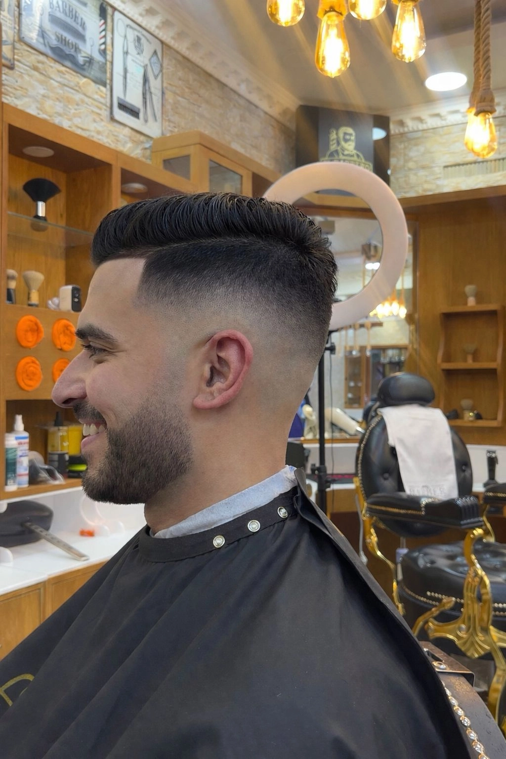 El barbero MB - Haar- und Hautpflegebehandlungen - Seitenansicht eines Mannes mit einem präzisen Skin Fade-Haarschnitt und gepflegtem Bart im Friseursalon.